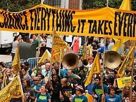 Sign that says "to change everything it takes everyone" carried by crowd in a march