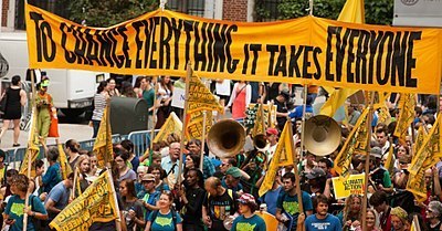 Sign that says "to change everything it takes everyone" carried by crowd in a march